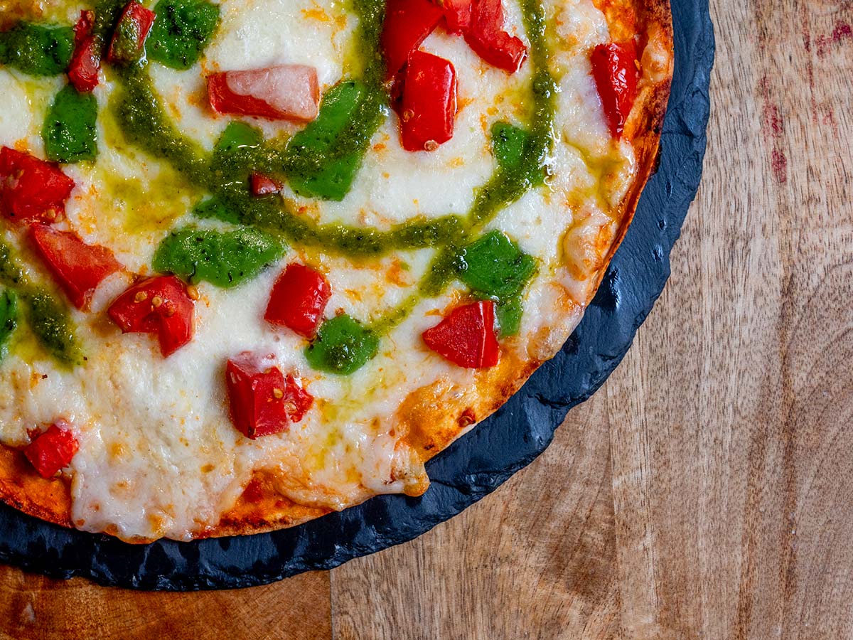 Pizza al pesto con tomate natural, queso al pesto, mozzarella y albahaca
