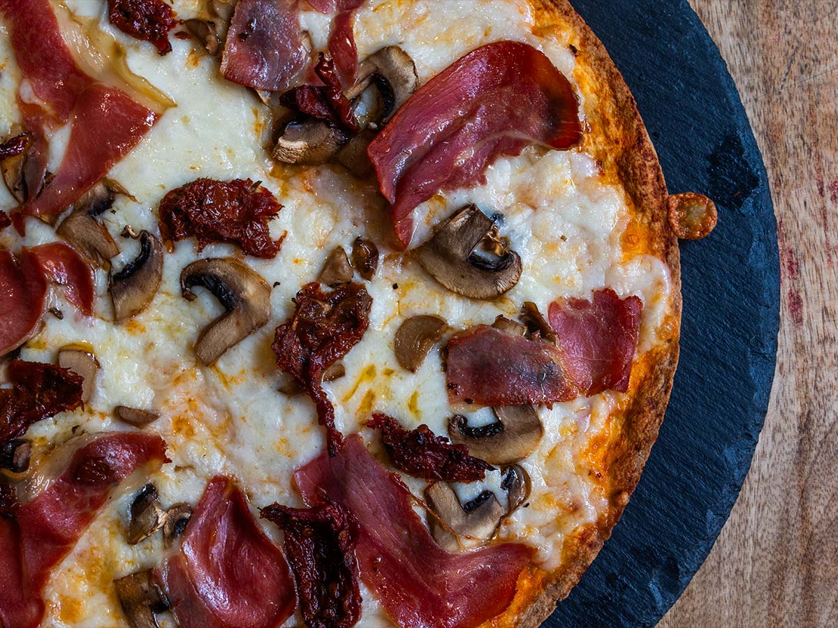 Pizza caprichosa con tomate seco, jamón, queso y champiñones